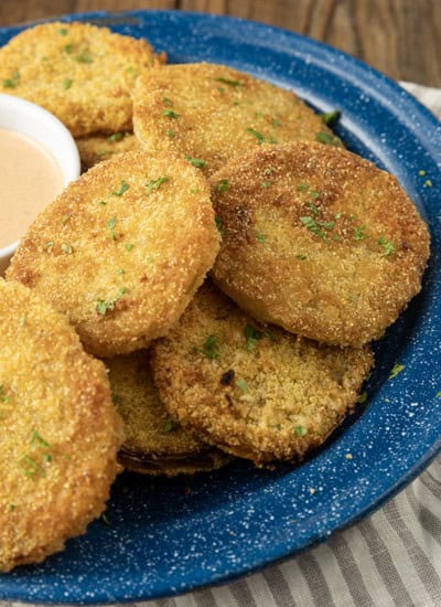 fried green tomatoes stacked on a blue enamel plate with a bowl of dip