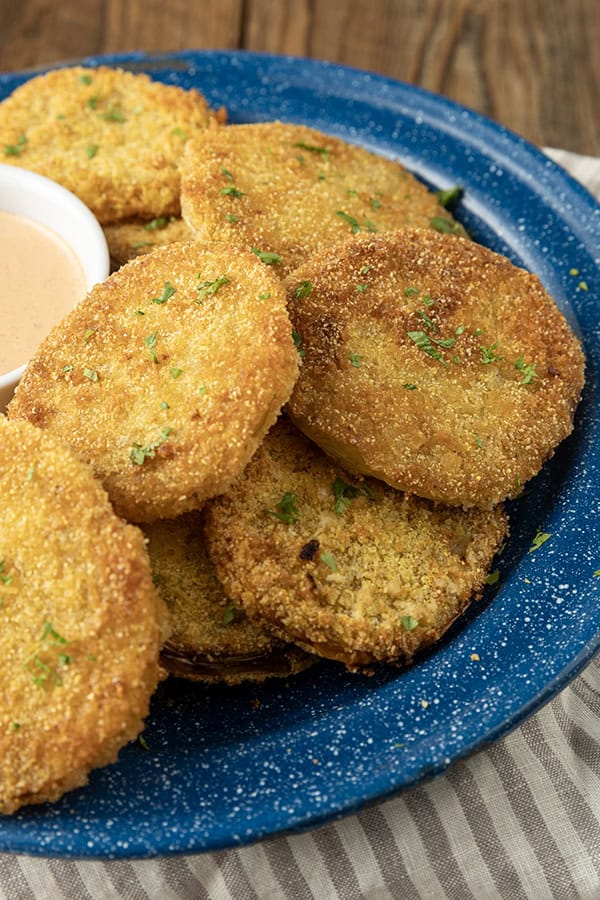 fried green tomatoes stacked on a blue enamel plate with a bowl of dip