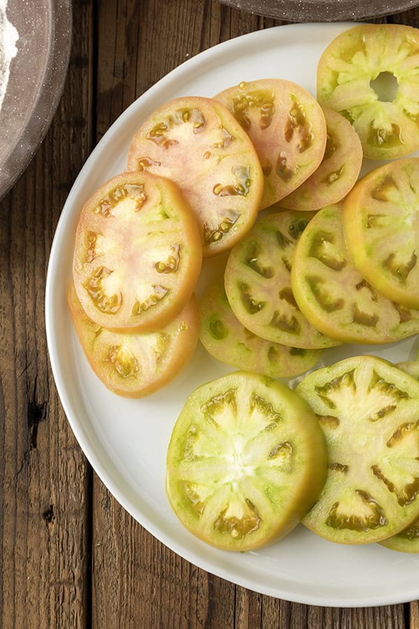 Sliced green tomatoes on a white plate on a rustic wooden table