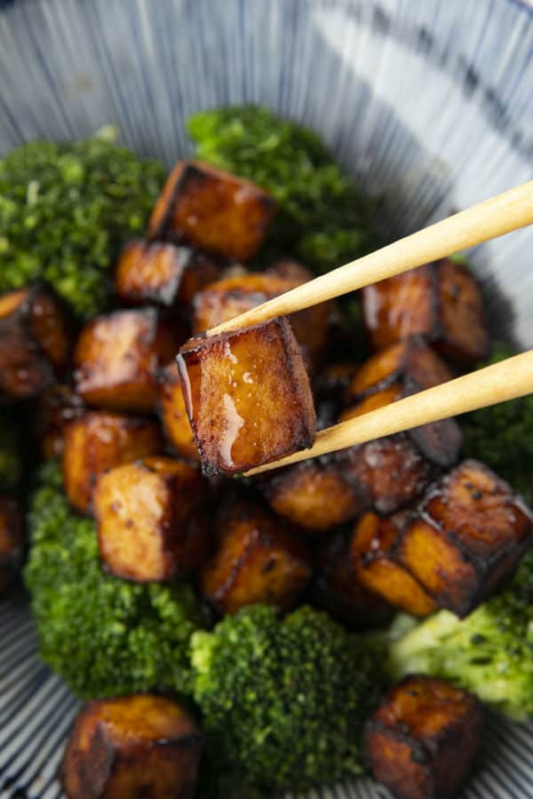 Crispy, golden brown cubes of air fryer tofu served with a drizzle of honey and broccoli on a blue and white striped oblong bowl.