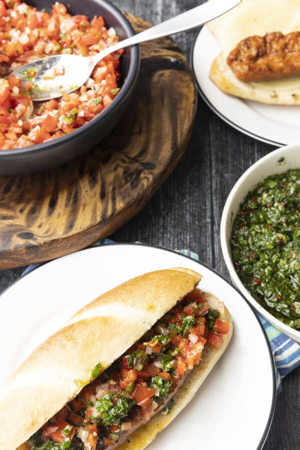 Choripan: Garlicky, spicy, smoky chorizo sausage is slowly grilled to perfection before being split, seared over high heat, and served on a bun with fresh chimichurri sauce and salsa a la criolla; the messier the better!