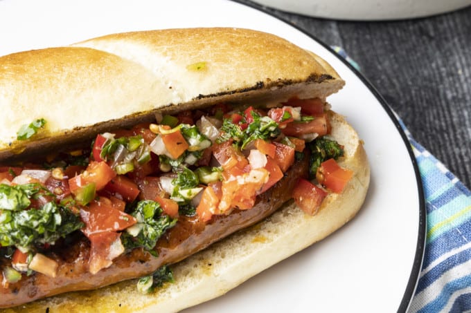 Choripan: Garlicky, spicy, smoky chorizo sausage is slowly grilled to perfection before being split, seared over high heat, and served on a bun with fresh chimichurri sauce and salsa a la criolla; the messier the better!