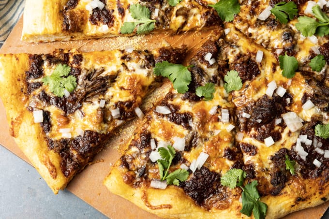 Birria Pizza: Chewy crust topped with tender shredded birria beef, smoky birria stew, loads of melted cheese, chopped sweet onion, fresh cilantro, a squeeze of fresh lime, and a bowl of red chile sauce for dipping. Imagine the best tacos you’ve ever tasted turned into a pizza and you have an idea just how fabulous this pizza is.