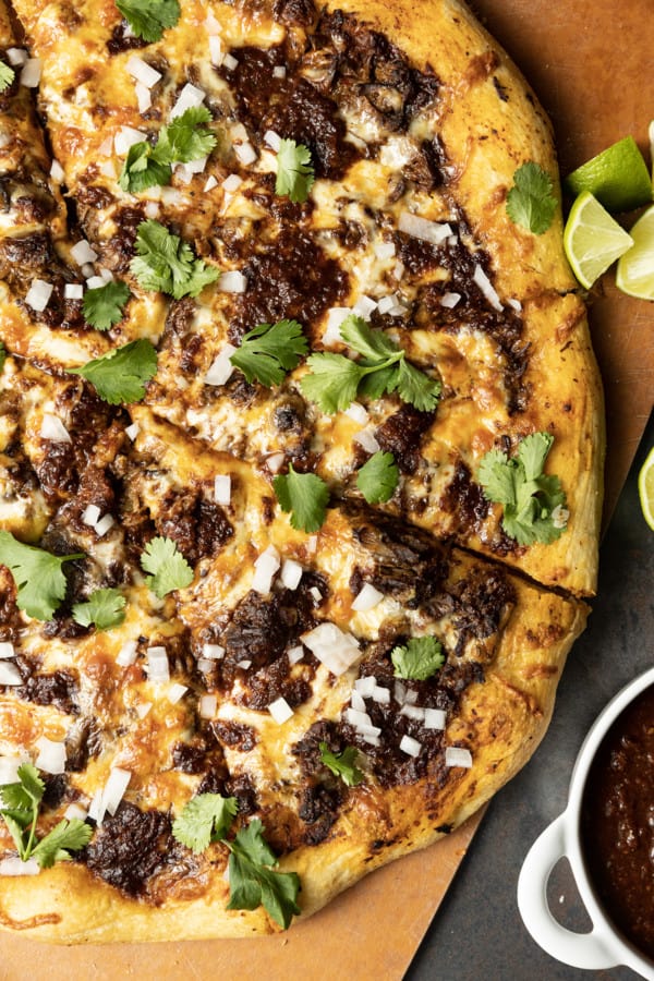 Birria Pizza: Chewy crust topped with tender shredded birria beef, smoky birria stew, loads of melted cheese, chopped sweet onion, fresh cilantro, a squeeze of fresh lime, and a bowl of red chile sauce for dipping. Imagine the best tacos you’ve ever tasted turned into a pizza and you have an idea just how fabulous this pizza is.