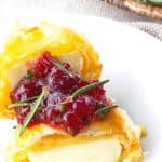 Bite sized baked brie in puff pastry with rosemary, pomegranate seeds, and sweet and spicy cranberry sauce.