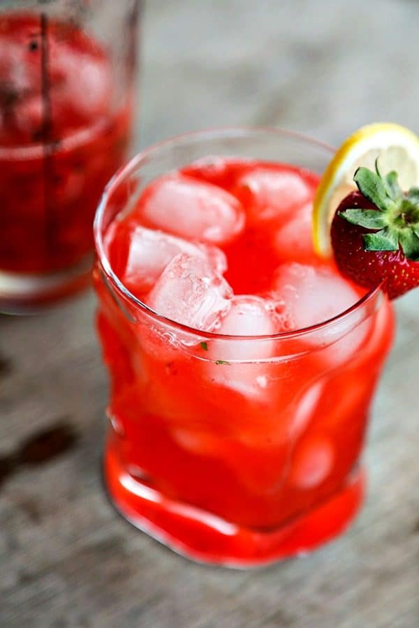 boozy strawberry basil lemonade, bormioli rocco sorgente highball glass, strawberry and lemon garnish, rustic wood table, vertical shot, glass cocktail shaker