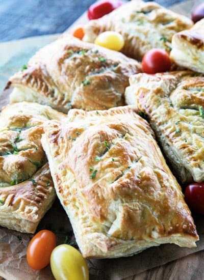 Breakfast Hot Pockets: puff pastry filled with cheesy scrambled eggs and sausage links on a cutting board with cherry tomatoes.