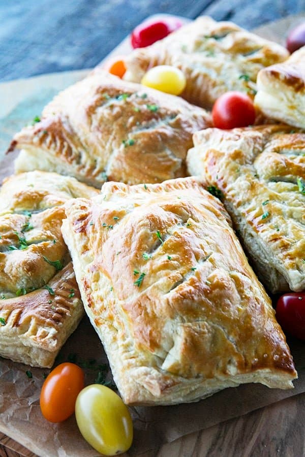 Breakfast Hot Pockets: puff pastry filled with cheesy scrambled eggs and sausage links on a cutting board with cherry tomatoes.