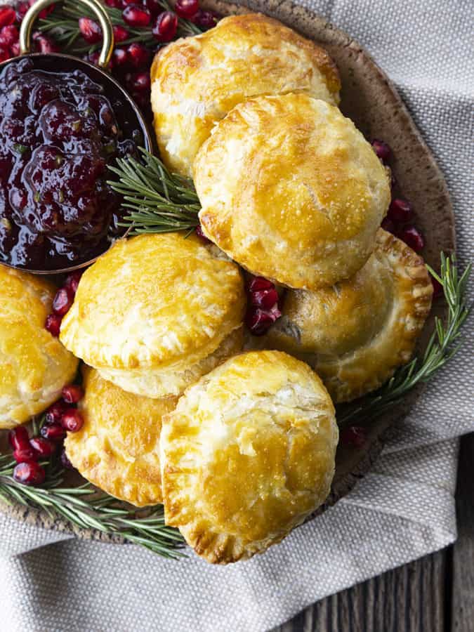 Bite sized baked brie in puff pastry with rosemary, pomegranate seeds, and sweet and spicy cranberry sauce.