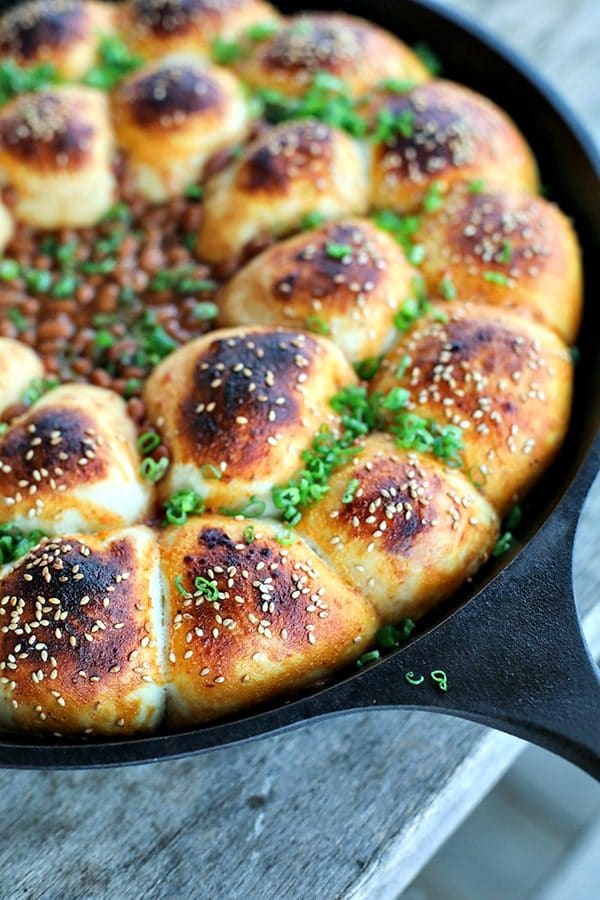 Cheeseburger Bombs Baked Bean Skillet is a whole host of comfort foods in one pan! Delicious rolls stuffed with melted Cheddar cheese and tender meatballs, baked in a cast iron skillet around barbecue baked beans. This is as good as game day food gets!