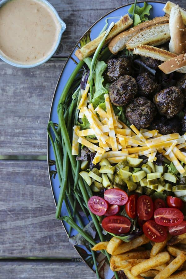 Cheeseburger Salad from foodiewithfamily.com with sesame bun croutons. grilled meatballs and green onions, cheese, pickles, tomatoes, and hot fries.