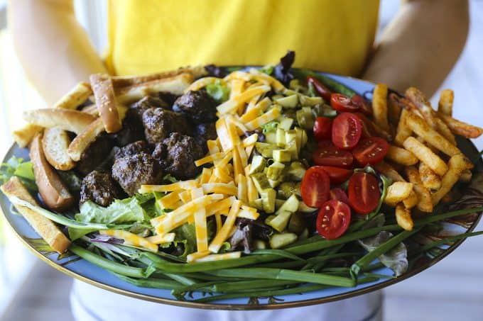 Cheeseburger Salad from foodiewithfamily.com with sesame bun croutons. grilled meatballs and green onions, cheese, pickles, tomatoes, and hot fries.