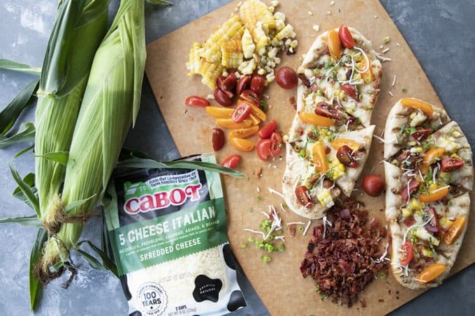 ear of corn, cutting board, bacon, cheese, tomato topped flatbread