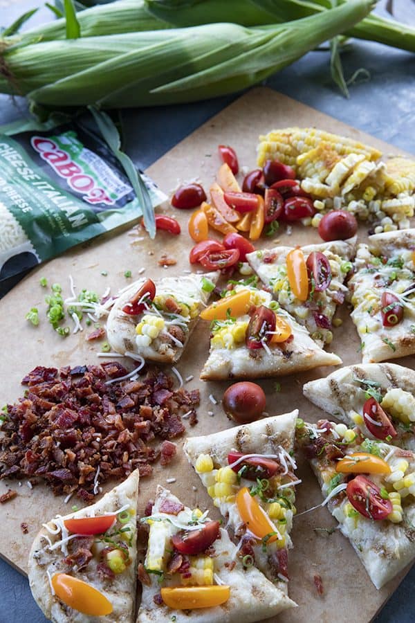 grilled flatbread with bacon, corn, tomatoes, and cheese on a cutting board