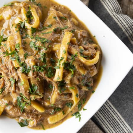 crock pot beef and noodles in a white square bowl on linens