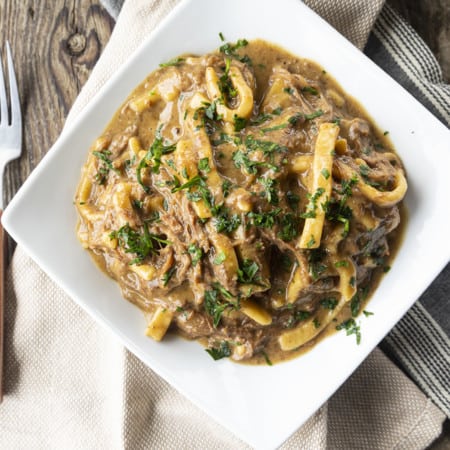 crock pot beef and noodles in a white square bowl on linens