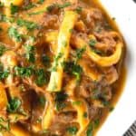 crock pot beef and noodles in a white square bowl on linens