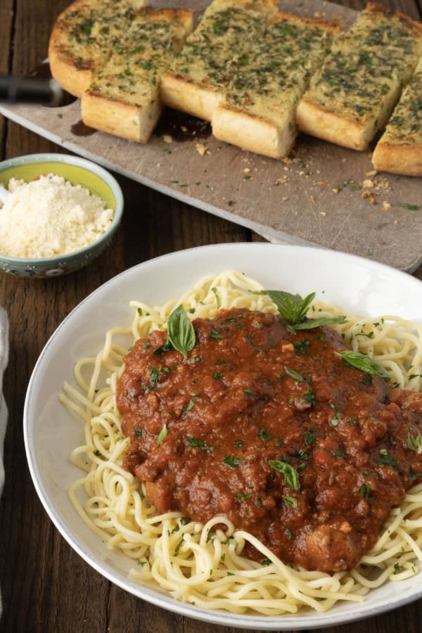 spaghetti sauce on spagetti on a plate topped by fresh herbs with a napkin and fork on the left.