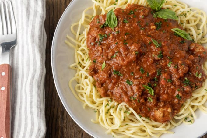 spaghetti sauce on spagetti on a plate topped by fresh herbs with a napkin and fork on the left.