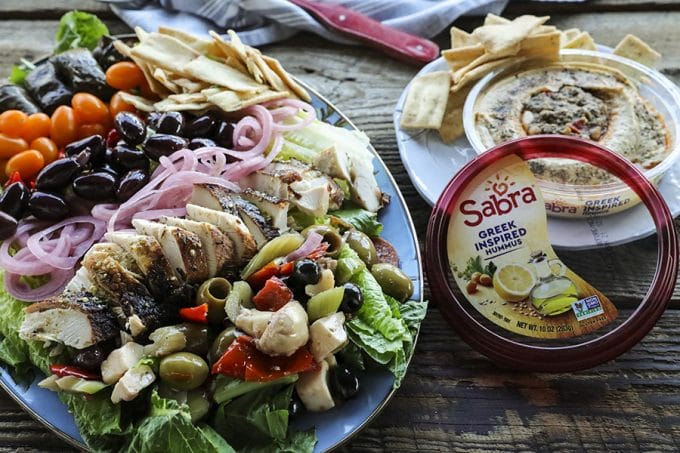 Greek Salad with lemon garlic chicken, marinated olive salad, quick pickled red onions, crumbled feta cheese, garlic stuffed kalamata olives, tiny grape tomatoes, stuffed grape leaves, Greek salad dressing, pita chips as croutons, and a hearty dollop of hummus. This salad will fill you up with sunshiny goodness without making you feel like a slug. The post includes instructions on how to pack these salads up to four days ahead of time for work-week and school lunches.