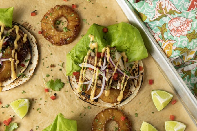 Make taco nights magical with jerk chicken tacos! Fresh lettuce leaves stacked on charred tortillas are piled high with juicy jerk chicken, grilled pineapple slices, diced bell peppers, thinly sliced onions, a drizzle of sauce or spoonful of mango salsa.