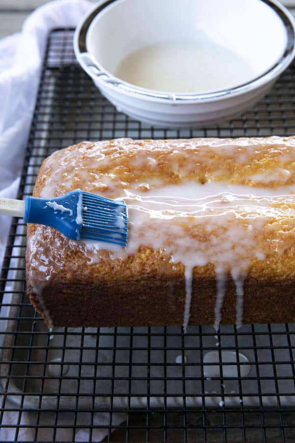 Glazing a French Grandma Lemon Yogurt Cake on a black cooling rack over a pan.