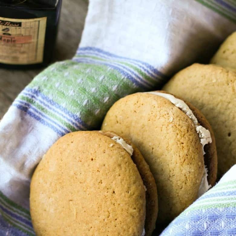 stack of Amish Maple Sandwch Cookies, whoopie pies, white towel with blue and green, antique maple extract bottle, wooden bench