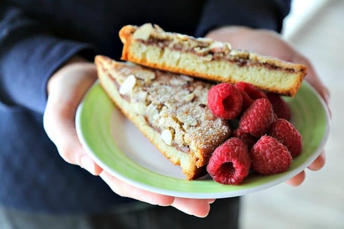 Nutella Raspberry Bostock on an antique white dessert plate with bright green rim, almond crusted, dusted with powdered sugar, raspberries on plate.