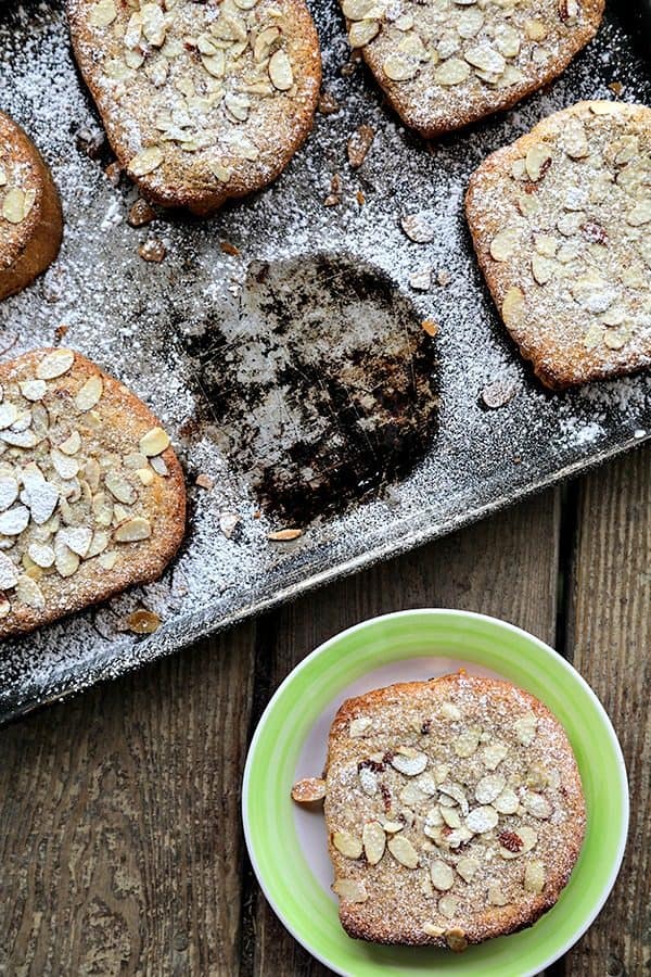 Antique Half sheet pan with Nutella Raspberry Bostock or brioche aux amandes, dusted with powdered sugar, one piece missing from the pan, one piece on an antique dessert plate with a bright green edge.