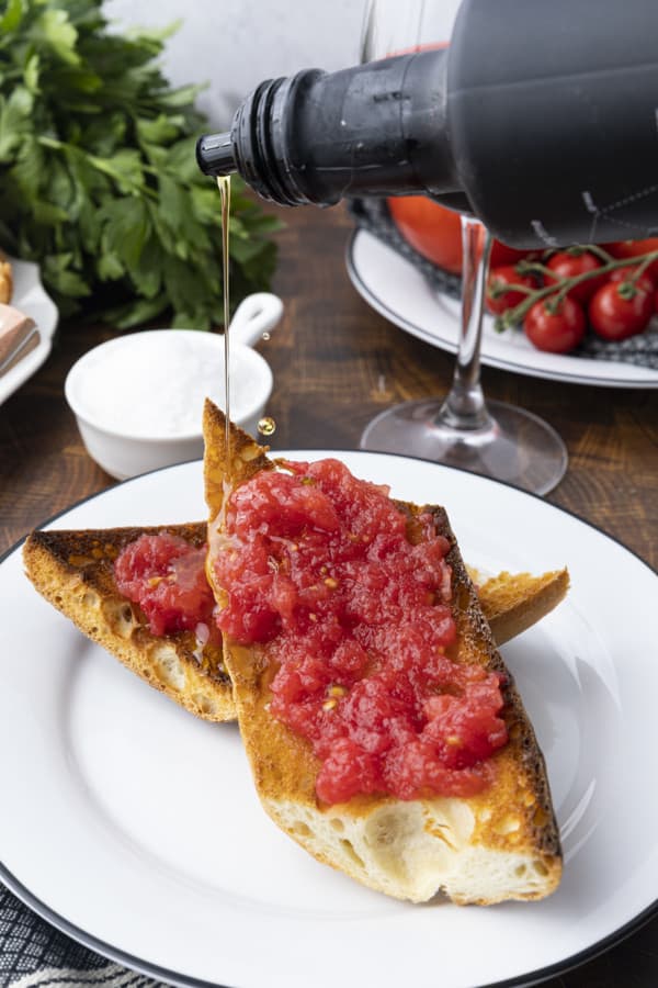 Sublime and simple Pan Con Tomate has just five ingredients; toasted rustic bread rubbed with a garlic clove, juicy fresh tomato pulp, extra-virgin olive oil, and coarse flaky sea salt. Also known as Spanish Tomato Bread, Pan Tumaca, or Pa Amb Tomàquet, this easy recipe using simple ingredients is equally at home served at a dinner party with a Spanish omelette or as part of a traditional Spanish breakfast.