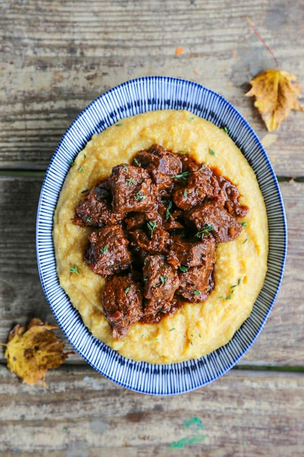 Tuscan Braised Beef in red wine sauce on creamy polenta in a blue and white dish.