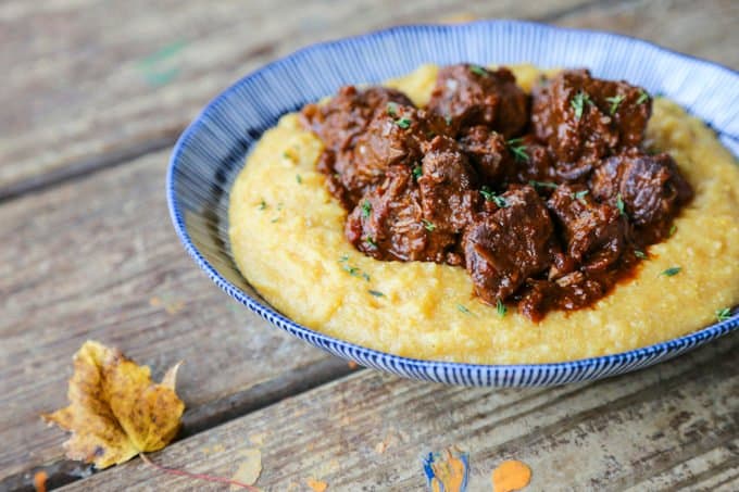 Tuscan Braised Beef in red wine sauce on creamy polenta in a blue and white dish.