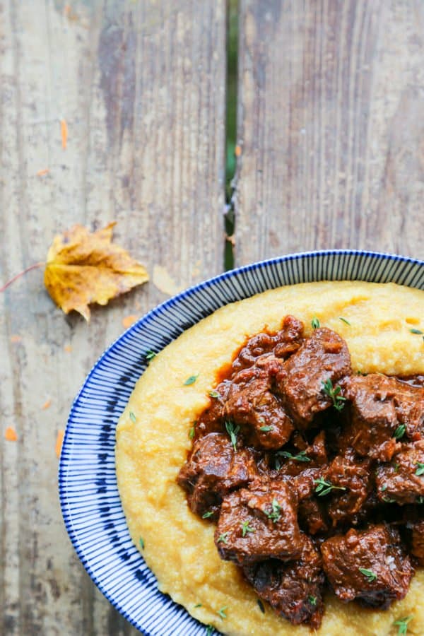 Tuscan Braised Beef in red wine sauce on creamy polenta in a blue and white dish.