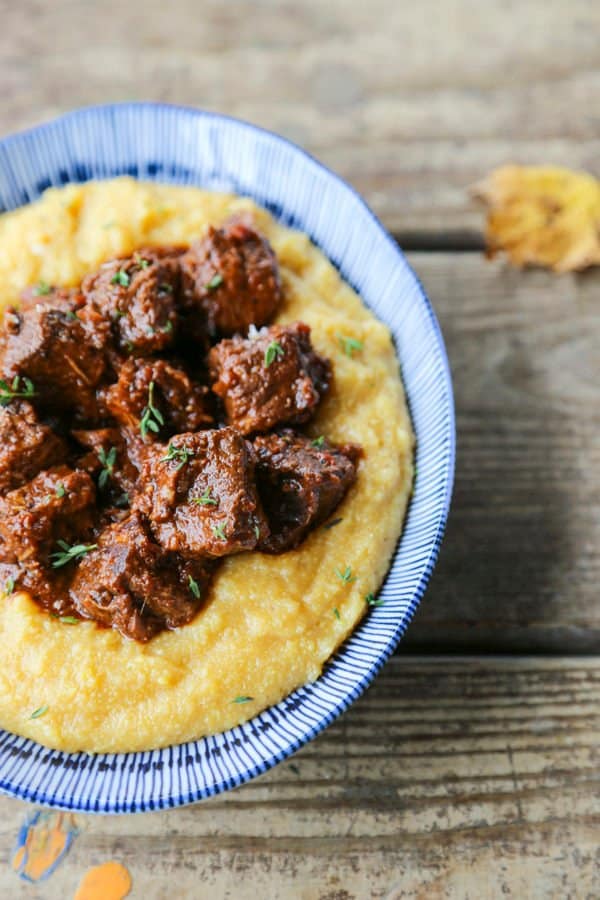 Tuscan Braised Beef in red wine sauce on creamy polenta in a blue and white dish.