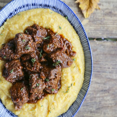 Tuscan Braised Beef in red wine sauce on creamy polenta in a blue and white dish.