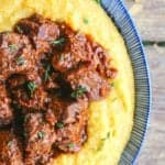 Tuscan Braised Beef in red wine sauce on creamy polenta in a blue and white dish.