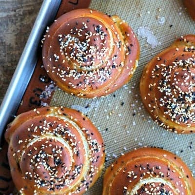 Soft pretzel rolls for sandwiches, silpat, half sheet pan, rustic wood table, sesame seeds, pretzel salt