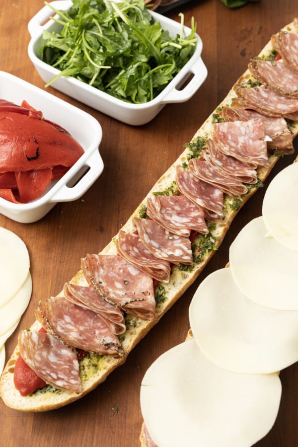 This is no ordinary Salami Sandwich; a crusty baguette is stuffed to bursting with a variety of salamis, roasted red pepper, pesto sauce, provolone cheese, fresh basil, and dressed arugula, then tightly wrapped and stashed in the refrigerator overnight. Then you can slice it all up and arrange it on a platter for a party or stretch it out for up to 5 days! And let me tell you, if you slice a little off of this every day for lunch with a cup of soup or bag of chips, you're going to feel very clever indeed. If you're feeling generous, pop it in a lunch bag for a school lunch that will make your kid the envy of the school.