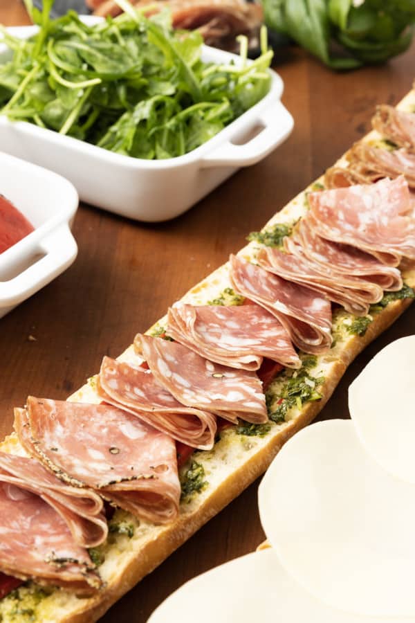 This is no ordinary Salami Sandwich; a crusty baguette is stuffed to bursting with a variety of salamis, roasted red pepper, pesto sauce, provolone cheese, fresh basil, and dressed arugula, then tightly wrapped and stashed in the refrigerator overnight. Then you can slice it all up and arrange it on a platter for a party or stretch it out for up to 5 days! And let me tell you, if you slice a little off of this every day for lunch with a cup of soup or bag of chips, you're going to feel very clever indeed. If you're feeling generous, pop it in a lunch bag for a school lunch that will make your kid the envy of the school.