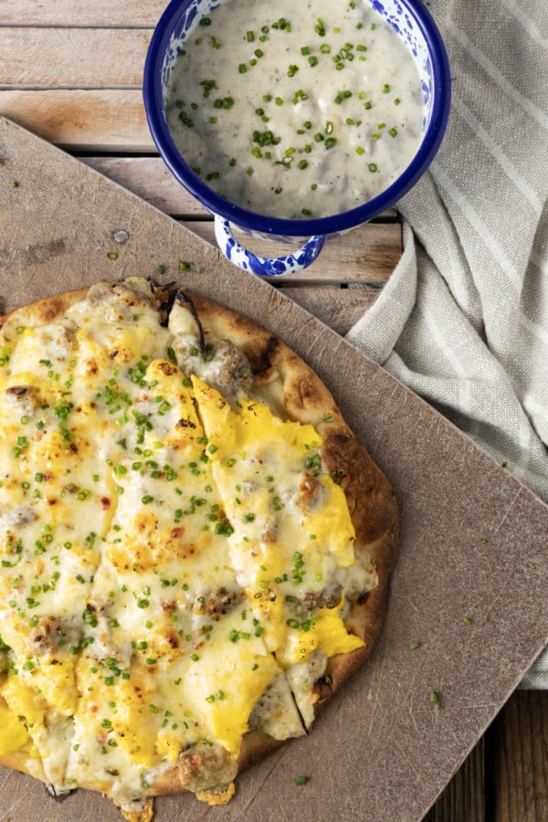 Hold onto your socks, because Sausage Gravy Breakfast Pizza just might knock them off! This ultimate comfort food mashup is coming soon to a breakfast, brunch (or dinner!) table near you. Chewy pizza crust is topped with cheesy, fluffy scrambled eggs, savoury, flavourful, creamy sausage gravy, and fragrant chives in this deliciously different pizza. Made on naan bread (or pre-baked pizza shells, homemade or purchased), these pizzas come together in just moments, too!