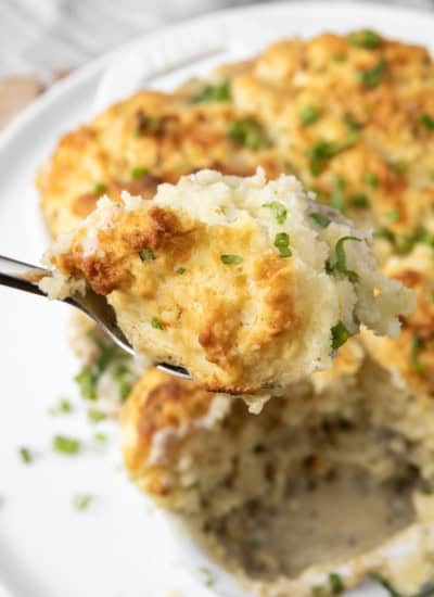 small white casserole dish filled with sausage gravy and topped with buttermilk biscuit crust on top of a plate with a spoon in it.