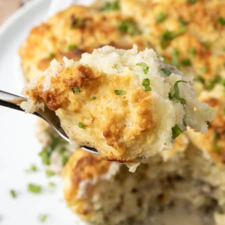 small white casserole dish filled with sausage gravy and topped with buttermilk biscuit crust on top of a plate with a spoon in it.