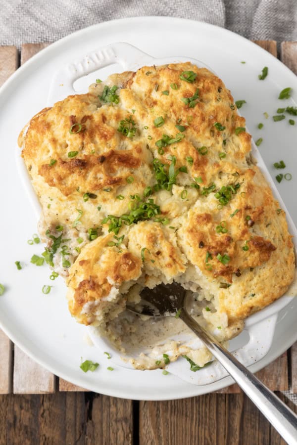 small white casserole dish filled with sausage gravy and topped with buttermilk biscuit crust on top of a plate with a spoon in it.