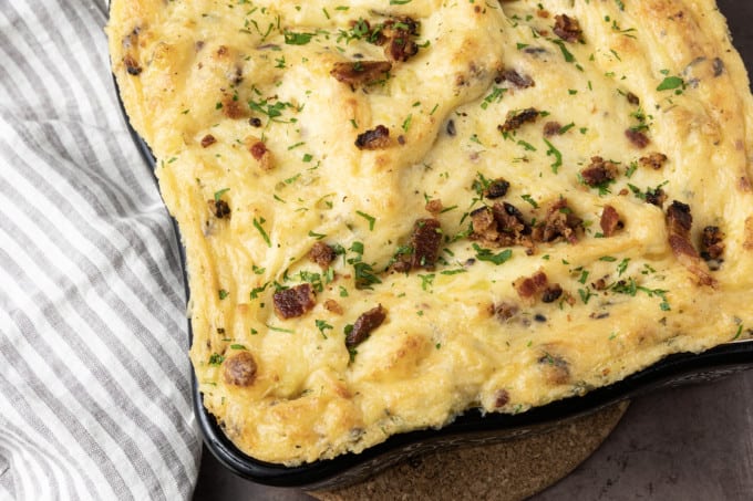 Get ready to dig into a baking dish filled with piping hot, irresistibly golden crusted, super creamy Twice Baked Mashed Potatoes. This make-ahead perfect side dish combines everything you love about creamy mashed potatoes, baked and twice baked potatoes; grated cheese, sour cream, crispy bacon, fresh herbs, and a whisper thin crispy crust at the edges. The only thing better than the taste of Twice Baked Mashed Potatoes casserole is its convenience. You can make it up to three days ahead of time and reheat before serving or you can make it, wrap it tightly, and freeze it for up to a month.